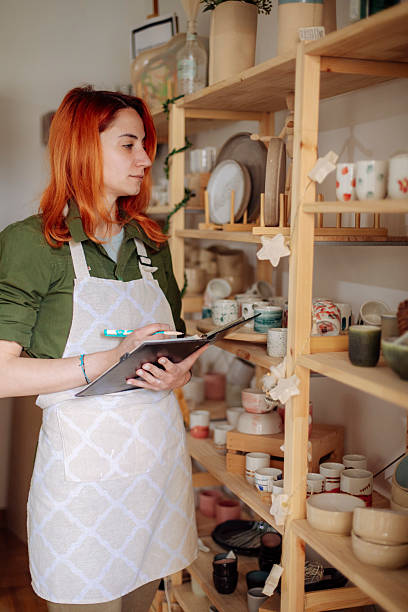istock Red-haired artist counting ceramic mugs in her atelier 2208471466