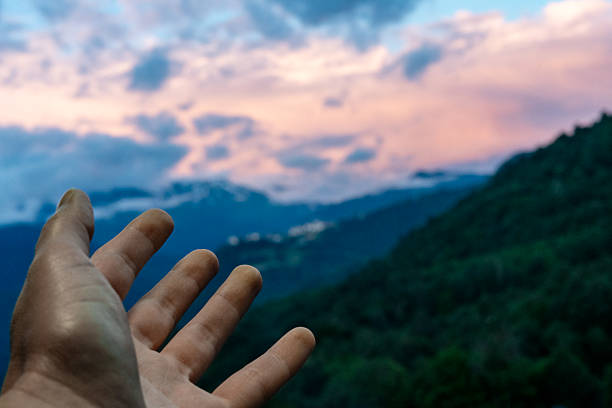 istock Outstretched hand reaching towards a distant landscape of mountains under cloudy sky at sunset, nature's beauty copy space 2208472852