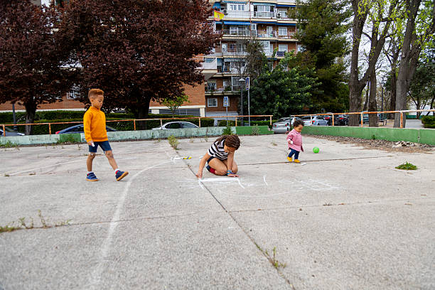 Three young children are enjoying their time drawing with chalk on the pavement of an outdoor playground