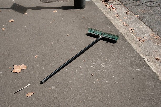 Black broom laying on the side of a road on a sunny day.