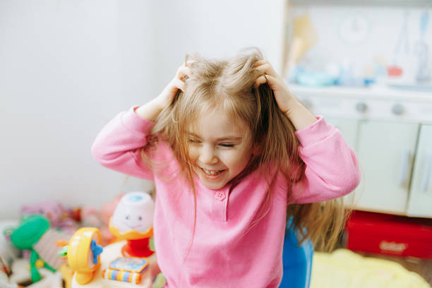 A cheerful girl with long hair pulls at her hair playfully while sitting in a colorful room filled with toys. The warm atmosphere highlights her joyful expression and playful energy.