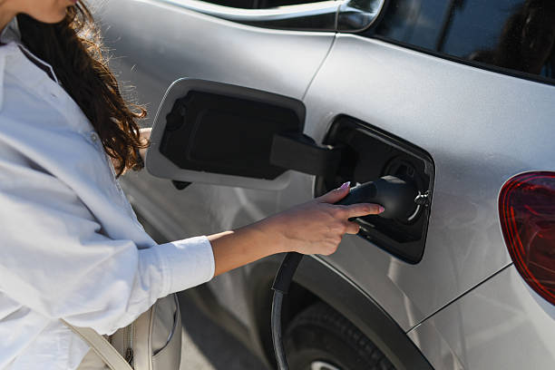 istock Female Plugging In Modern Electric Vehicle at Charging Station 2208485143
