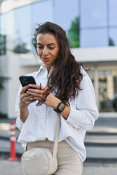 istock Attractive Female Messaging on Her Phone While Standing in Front of Modern Building 2208486725