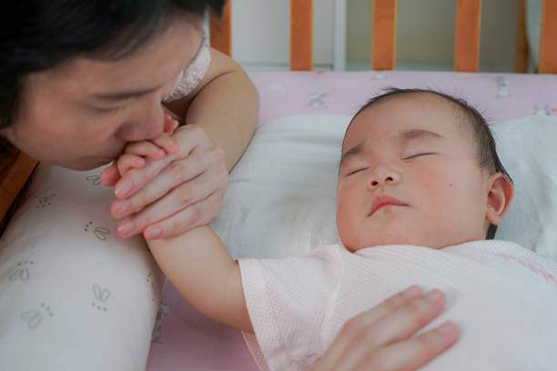 istock Mother Gently Kissing Her Sleeping Baby’s Hand in a Crib 2208486829
