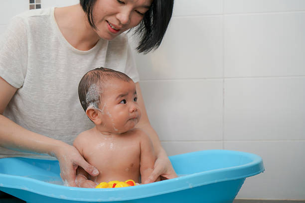 A warm and candid moment of a mother bathing her baby in a small plastic tub, playing together with rubber duck toys and enjoying gentle bonding time.