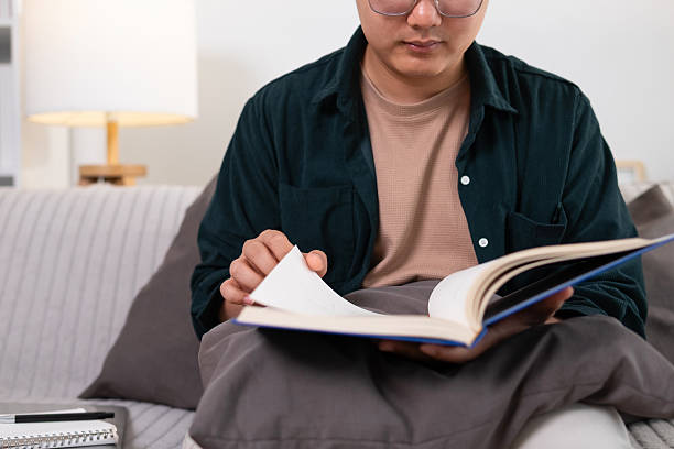 istock A young man sits and reads a blue book on the sofa. 2208487209