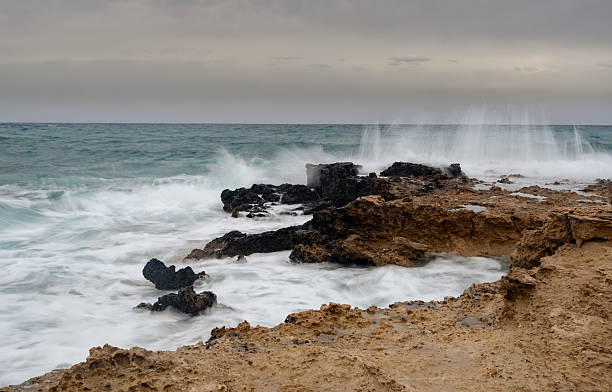 Ocean waves crashing against rocks on a stormy day, creating dramatic splashes and white foam