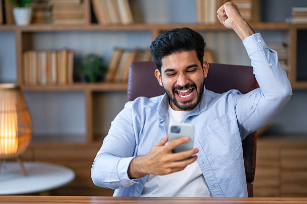 istock Handsome man using smartphone at the office very happy and excited, winner expression celebrating victory screaming with big smile and raised hands 2208489684