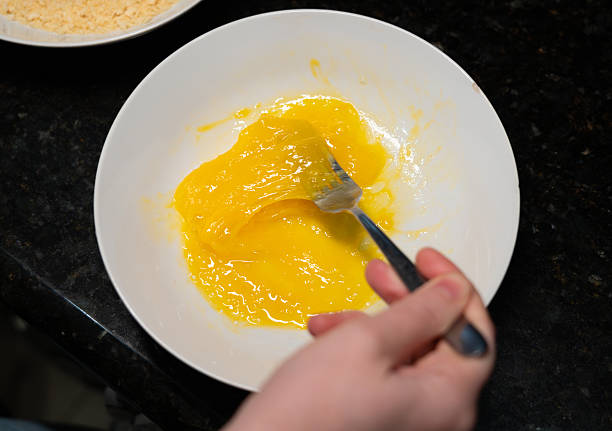 istock Female hands beat eggs with fork in a bowl, homemade schnitzel cooking process closeup 2208492397