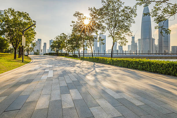 Empty stone pavement road with cityscape and trees during sunrise in Shenzhen.