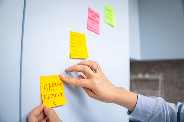 Creative individual attaching a colorful sticky note with a birthday message on a fridge in a modern kitchen environment