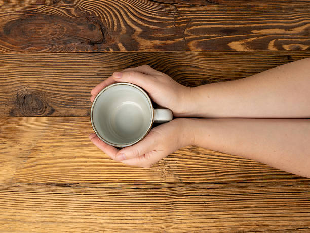 istock Hand Holds Cup, Empty Cup in Hands, Coffee Mug, Teacup Mockup, Cup in Arms on Wooden Table 2208508979