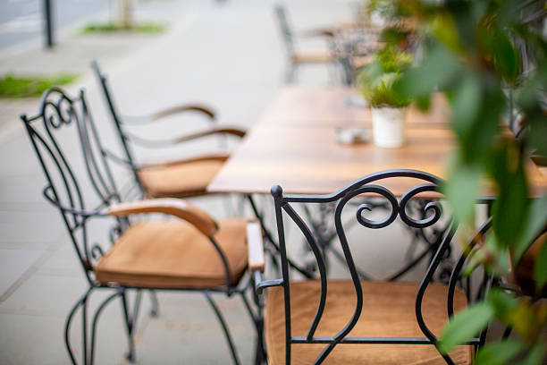 Close-up on stylish wrought iron chairs and wooden table outdoors. Street cafe in downtown.