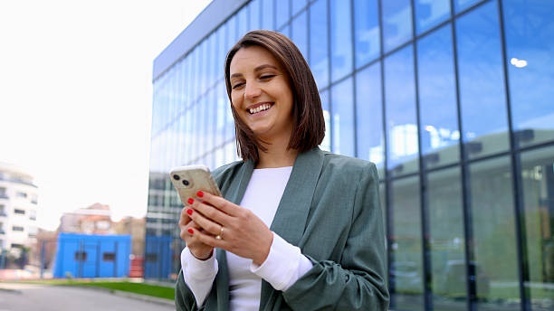 istock Smiling businesswoman using smartphone in front of modern office building 2208520270