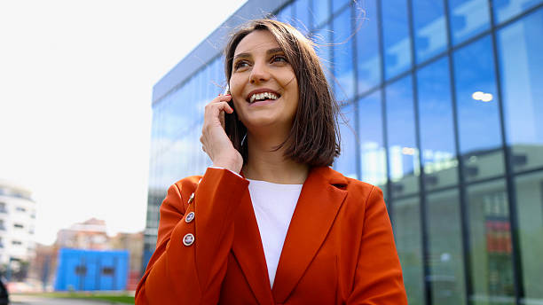 istock Businesswoman smiling while talking on phone in front of modern office building 2208520357