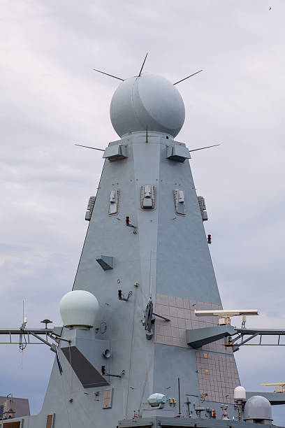 istock Close-up of a modern naval warship's radar tower with advanced surveillance and communication systems against a cloudy sky. 2208526496