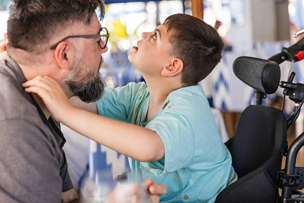 Child with cerebral palsy joyfully hugging father while sitting together at a restaurant table, sharing a special mealtime experience