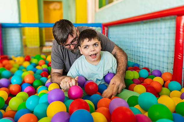 Father and son with cerebral palsy playing together in ball pit