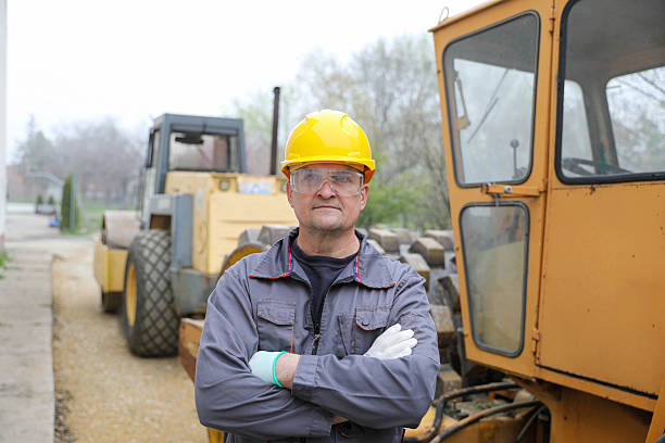 A middle-aged male engineer wearing a yellow hard hat and safety gear, captured in a close-up portrait. Concept: Road construction machinery.