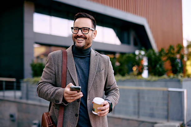 istock Smiling businessman walking and using smartphone while holding coffee 2208538803