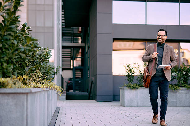 istock Smiling businessman walking outside office building holding tablet 2208538855