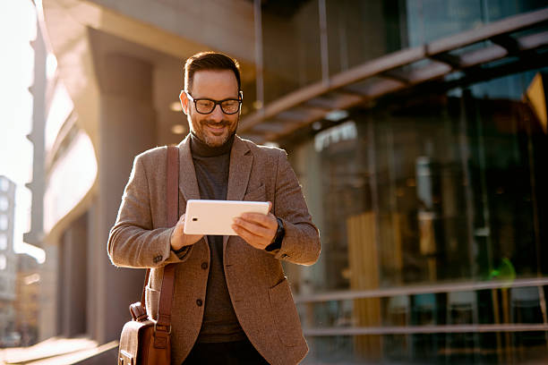 istock Smiling businessman using digital tablet while walking in the city 2208538856