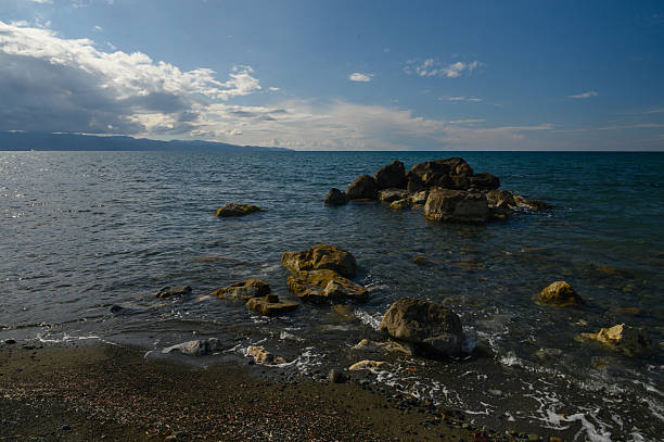 istock Vibrant coastal tranquility where waves gently caress the rugged rocks under a vast blue sky at midday in a serene seaside landscape 2208540044