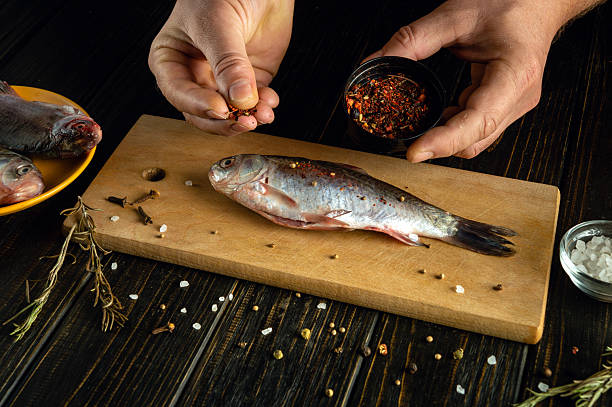 istock A person seasons a freshly caught fish with various spices and herbs, preparing it for cooking. Nearby, more fish and ingredients are visible on the table 2208542814