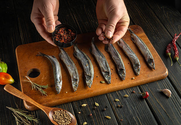 istock Fresh fish is arranged on a wooden cutting board, while hands add spices from a small bowl. Chili peppers, herbs, and tomatoes surround the preparation area, creating a cozy atmosphere 2208542839