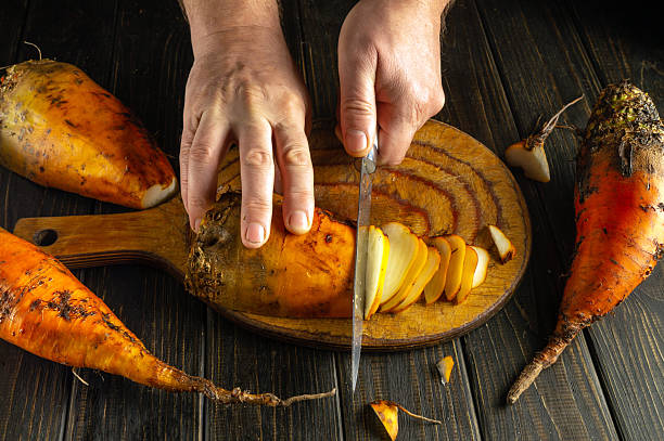 istock Hands chop orange root vegetables on a wooden cutting board with a sharp knife. The rustic kitchen features earthy tones and highlights the preparation of wholesome, healthy food 2208542955