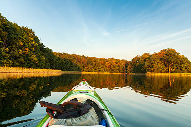 Kayak gliding across a tranquil lake, trees and reeds bathed in the golden light of the setting sun.