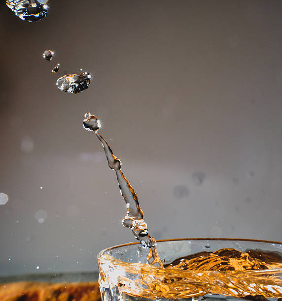 A drop splashing in orange water, falling into the water against a gray background sparking