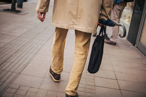 Back view of a senior man lower part of body walking on the street. He wears ocher pants and an ocher jacket.