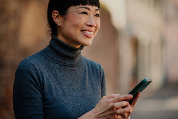 istock Smiling mature woman using smartphone on city street 2208545189