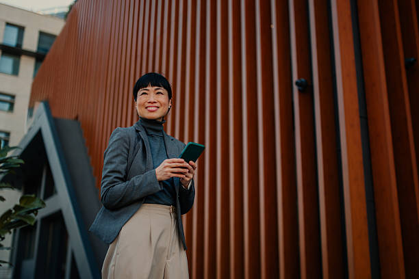 istock Smiling businesswoman using smartphone outside modern office building 2208545197