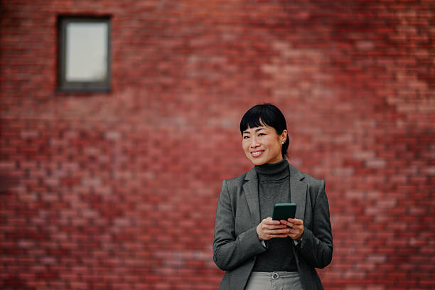 istock Smiling businesswoman using smartphone in front of red brick wall 2208545247