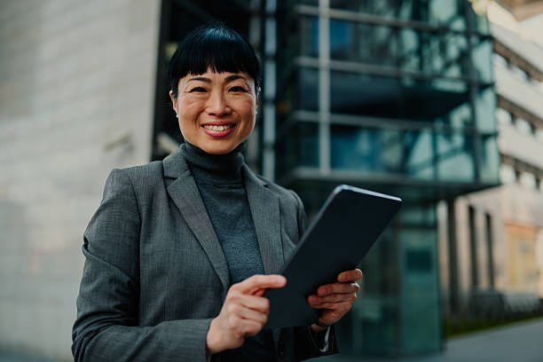 istock Smiling businesswoman using digital tablet outside office building 2208545261