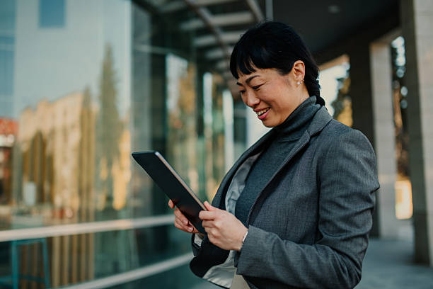istock Smiling businesswoman using digital tablet outside office building 2208545267