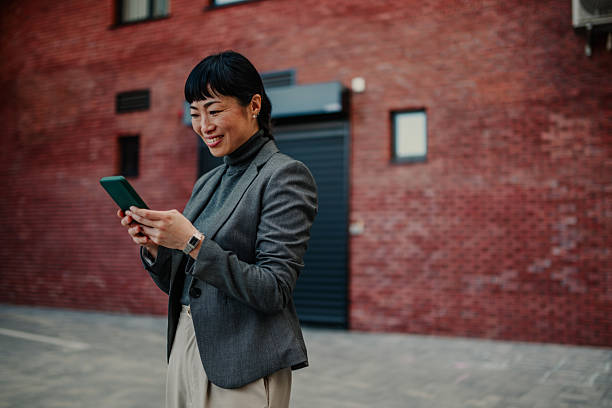 istock Smiling asian businesswoman using smartphone in urban setting 2208545280