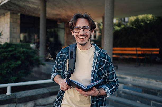 istock Smiling university student holding a book and wearing a backpack 2208545820