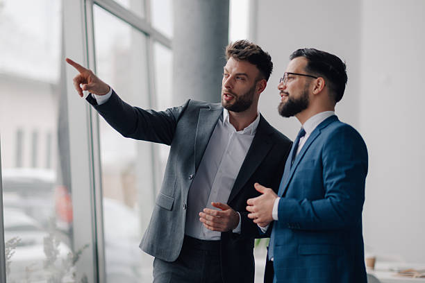 istock Two businessmen planning strategy while looking out office window 2208547881
