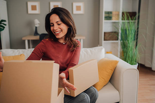 istock Woman opening cardboard boxes at home on sofa, feeling happy 2208551205