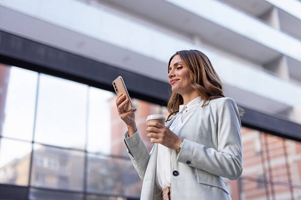 istock Businesswoman using smartphone and drinking coffee outdoors 2208551285