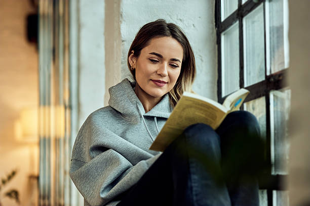 istock Woman Sitting by Window Reading a Book in a Cozy Urban Setting 2208552791