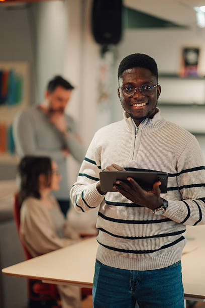 istock Young businessman using tablet in modern office with colleagues working in background 2208554332