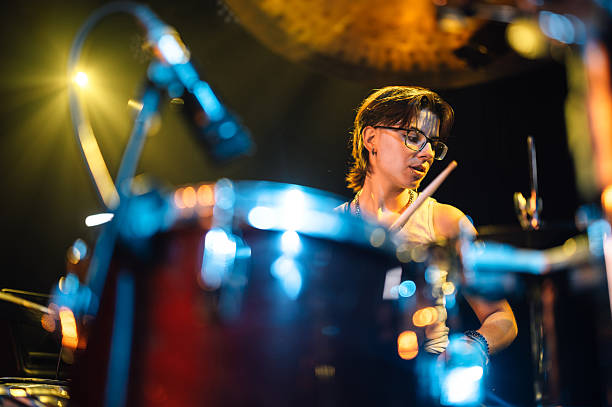Woman musician playing drums during a live performance under stage lights