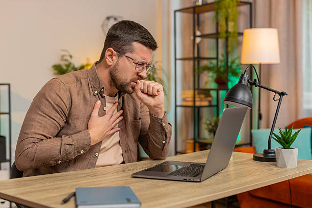 istock Sick man freelancer feeling unwell suffering from sore throat touches chest while coughing at home 2208561899