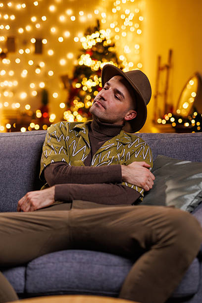 istock Relaxed man sitting on a cozy couch with festive holiday lights behind 2208562055