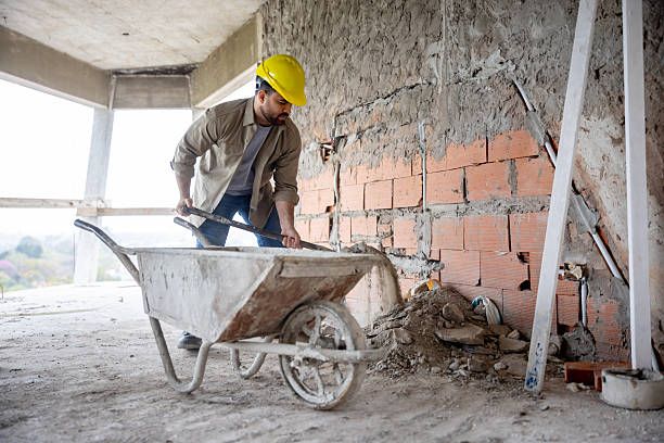 Latin American construction worker shoveling debris into a wheelbarrow at a building site - people at work concepts