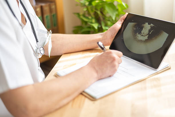 istock Female doctor in white coat with stethoscope is writing notes on clipboard while examining ultrasound scan displayed on tablet computer, focusing on healthcare and medical diagnosis 2208598258